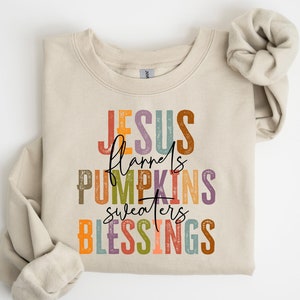 May include: A beige sweatshirt with the text "JESUS flannels PUMPKINS sweaters BLESSINGS" in colorful, vintage-style lettering.