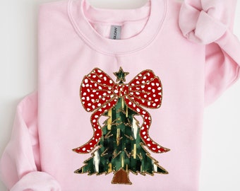 May include: Pink sweatshirt with a green Christmas tree design with a red and white polka dot bow. The tree is decorated with gold glitter.