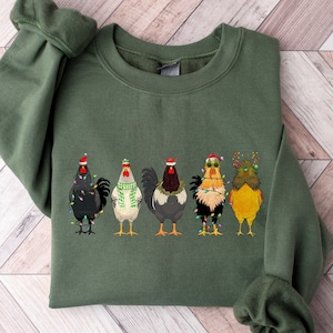 May include: A green sweatshirt with a festive design of five chickens wearing Christmas hats and lights. The chickens are in a row, facing forward, and have different colored feathers.
