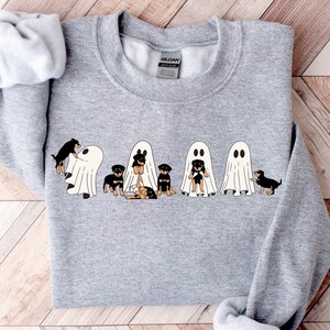 Op de afbeelding: Een grijs sweatshirt met een afbeelding van vijf zwarte en bruine honden die verkleed zijn als geesten voor Halloween.