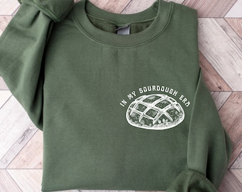 May include: A green sweatshirt with the text "In my sourdough era" and a white illustration of a sourdough bread loaf.