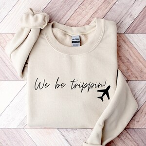May include: A beige sweatshirt with the text "We be trippin!" and a black airplane graphic.