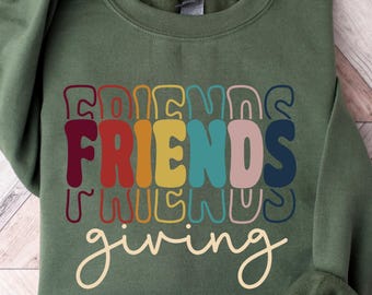 Könnte beinhalten: Ein olivgrünes Sweatshirt mit den Worten "FRIENDS giving" in einer Retro-Schriftart. Das Wort "FRIENDS" ist vertikal in Rot-, Orange-, Gelb-, Türkis-, Rosa- und Marineblautönen gestapelt.
