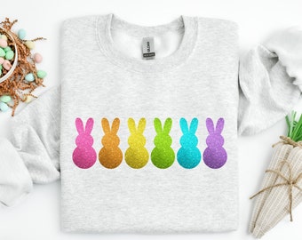 Könnte beinhalten: Ein graues Sweatshirt mit einer Reihe von sechs bunten Glitzer-Hasen-Silhouetten. Die Hasen sind rosa, orange, gelb, grün, blau und lila.