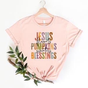 May include: A pink t-shirt with the text "JESUS flannels PUMPKINS sweaters BLESSINGS" in colorful, layered lettering.