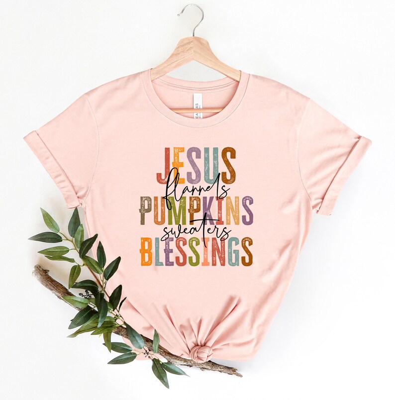 May include: A pink t-shirt with the text "JESUS flannels PUMPKINS sweaters BLESSINGS" in colorful, layered lettering.