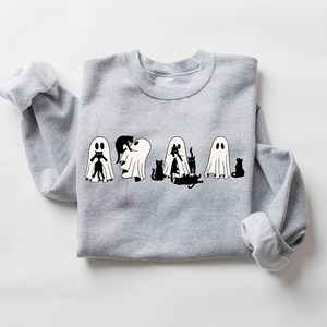 May include: A grey sweatshirt featuring a black and white graphic of ghosts and cats. The ghosts are dressed as cats, with the cats peeking out from underneath.