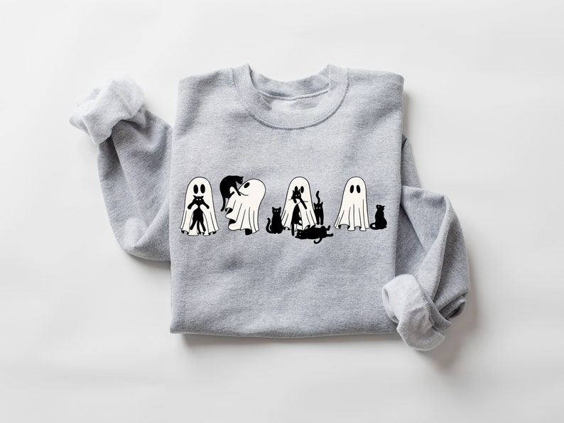 May include: A grey sweatshirt featuring a black and white graphic of ghosts and cats. The ghosts are dressed as cats, with the cats peeking out from underneath.