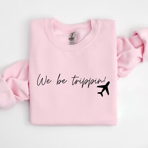 May include: Pink sweatshirt with the text "We be trippin!" and a black airplane graphic.
