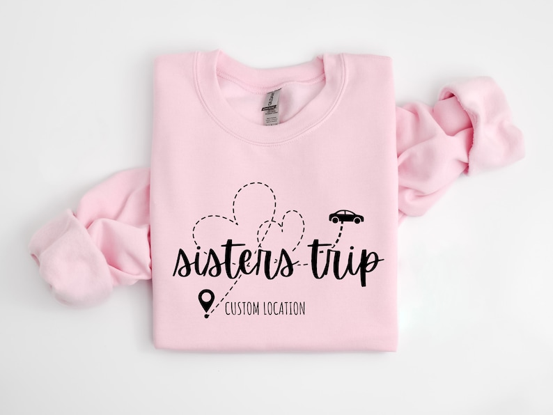 May include: Pink sweatshirt with a black graphic design that says "sisters-trip" with a car and a pin that says "custom location".
