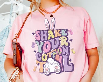 Könnte beinhalten: Pinkes T-Shirt mit einem Aufdruck eines Hasen mit dem Text "Shake Your Cotton Tail" in bunten, Retro-Lettern.