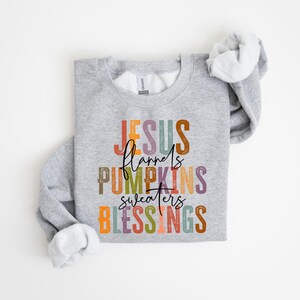May include: A gray sweatshirt with the text "JESUS flannels PUMPKINS sweaters BLESSINGS" in colorful letters.