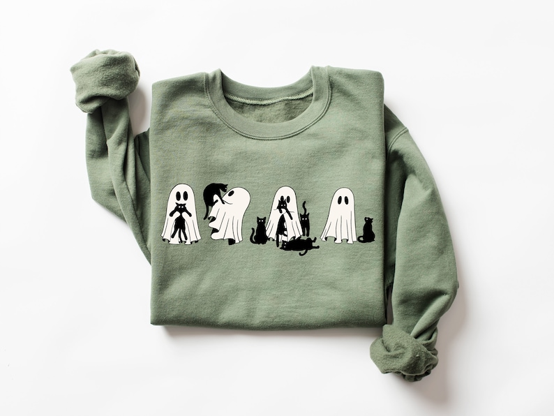 May include: A green sweatshirt featuring a white graphic of ghosts and black cats. The ghosts are wearing the cats as costumes.