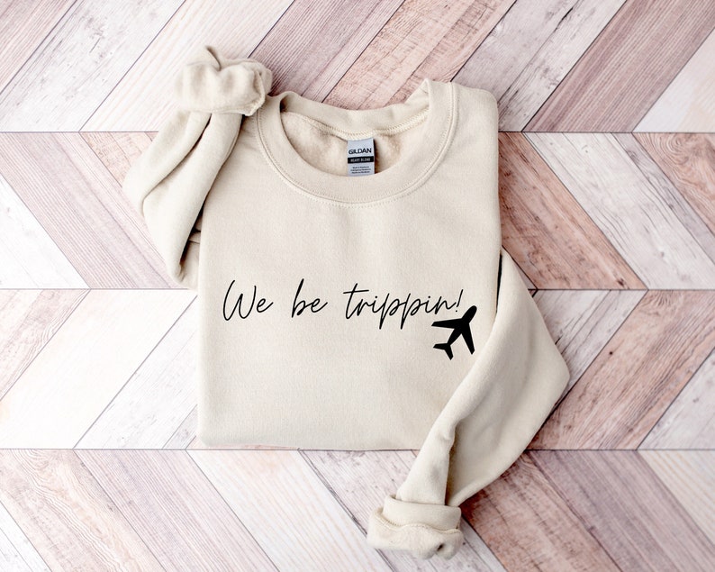 May include: A beige sweatshirt with the text "We be trippin!" and a black airplane graphic.