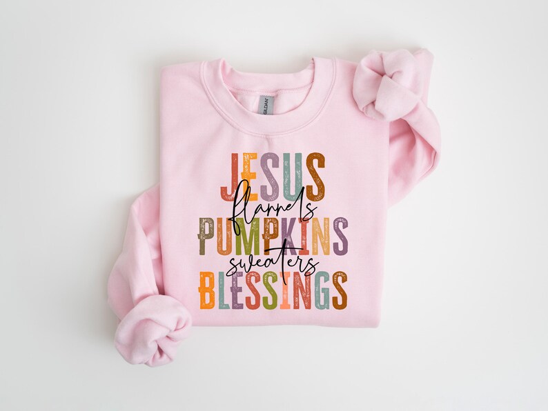 May include: Pink sweatshirt with the text "JESUS flannels PUMPKINS sweaters BLESSINGS" in colorful, distressed lettering.