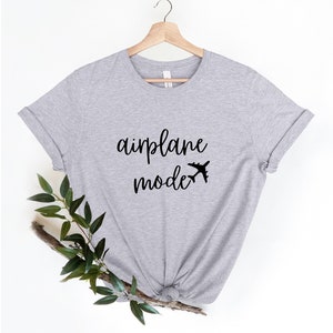 Puede incluir: Una camiseta gris con el texto "modo avi&oacute;n" y un peque&ntilde;o avi&oacute;n impreso en la parte delantera.