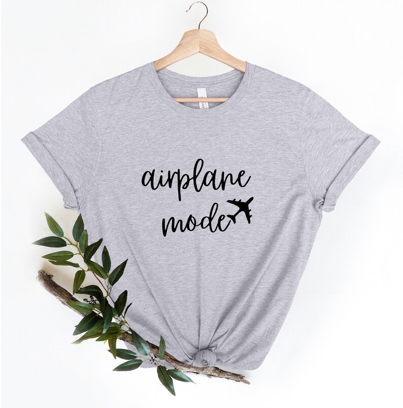 Puede incluir: Una camiseta gris con el texto "modo avi&oacute;n" y un peque&ntilde;o avi&oacute;n impreso en la parte delantera.