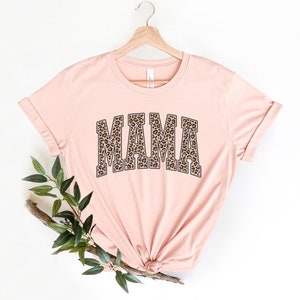 May include: A pink t-shirt with a leopard print "MAMA" graphic. The shirt is on a hanger and has a relaxed fit.