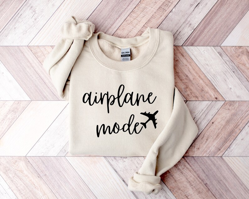 Puede incluir: Una sudadera beige con el texto "airplane mode" en letras cursivas negras y un peque&ntilde;o gr&aacute;fico de avi&oacute;n.