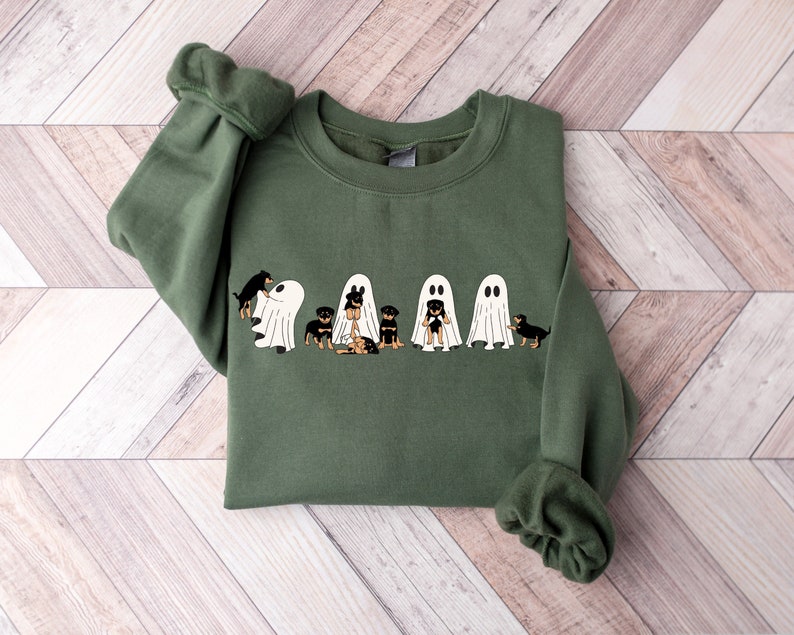 Op de afbeelding: Een groen sweatshirt met een afbeelding van vijf zwarte en bruine honden die verkleed zijn als spoken voor Halloween.