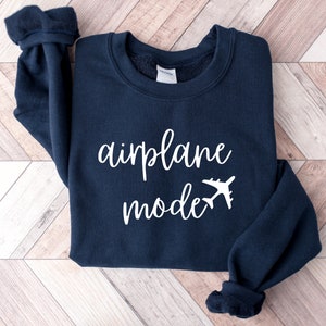 Puede incluir: Una sudadera azul marino con el texto "modo avi&oacute;n" en letras blancas y un gr&aacute;fico de avi&oacute;n blanco.