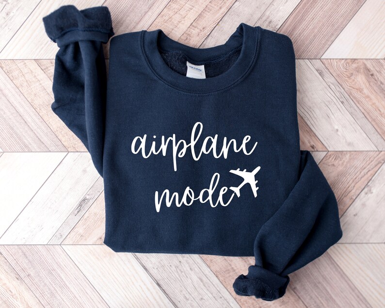 Puede incluir: Una sudadera azul marino con el texto "modo avi&oacute;n" en letras blancas y un gr&aacute;fico de avi&oacute;n blanco.