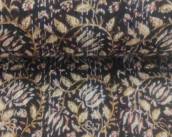 May include: A rolled-up, dark brown fabric with a repeating floral pattern in cream, tan, and burgundy. The fabric is stitched with white thread, creating a quilted effect. The design features stylized leaves and flowers.