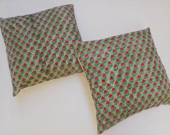 May include: Two green and red floral patterned throw pillows with white piping.