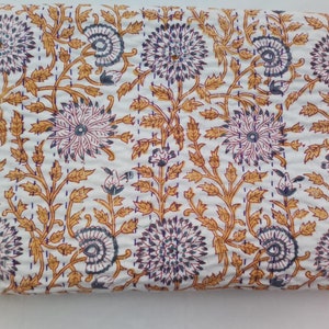 Pode incluir: Tecido branco com um padrão floral repetido em tons de roxo, azul e dourado. O design apresenta grandes flores estilizadas e vinhas de conexão. O tecido é provavelmente um edredom ou um cobertor.