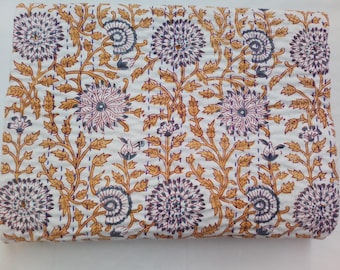 May include: White fabric with a repeating floral pattern in shades of purple, blue, and gold. The design features large, stylized flowers and connecting vines. The fabric is likely a quilt or blanket.