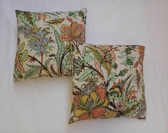 May include: Two cream-colored pillow covers with a floral pattern in shades of green, orange, and brown. The floral pattern features large flowers and leaves.