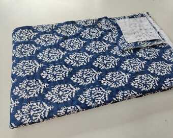 Puede incluir: Una colcha kantha azul y blanca con un patrón floral. La colcha está doblada por la mitad y tiene un respaldo blanco.