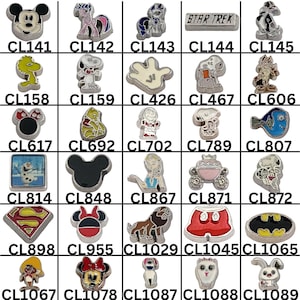 May include: A collection of silver-toned charms featuring various cartoon characters and symbols. Designs include Mickey Mouse, Snoopy, Superman logo, and a Star Trek logo. Each charm has a unique design and a corresponding number.