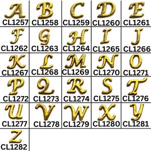 May include: A grid of gold-colored metal alphabet letters, each with a unique cursive design. Each letter is labeled with a corresponding code number. The letters are arranged in rows and columns, showcasing the entire alphabet.