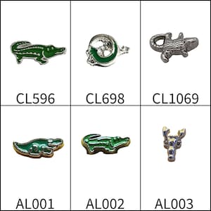 May include: A collection of six small metal charms featuring various designs. The items include green and silver alligator shapes labeled CL596, AL001, and AL002, a green and silver circular charm labeled CL698, a silver alligator labeled CL1069, and a silver lobster labeled AL003.