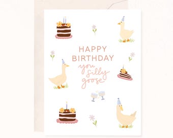 May include: A white birthday greeting card featuring illustrations of geese wearing blue striped party hats, chocolate cakes with candles, small flowers, and two clinking glasses. The text reads: HAPPY BIRTHDAY you silly goose.