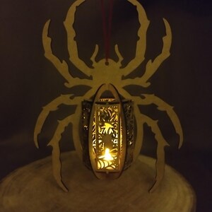 May include: A wooden spider-shaped lantern with a candle inside. The lantern is made of laser-cut wood and has a delicate design. The spider is hanging from a red string.