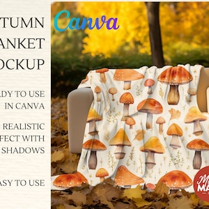 May include: A white throw blanket with a watercolor pattern of mushrooms in shades of orange, yellow, and brown. The blanket is draped over a beige couch and surrounded by autumn leaves.