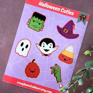Może przedstawiać: Arkusz naklejek o tematyce Halloween z kreskówkowymi ilustracjami potwora Frankensteina, kapelusza czarownicy, ducha, wampira, cukierków kukurydzianych, dyni i ręki zombie. Widoczny jest tekst "Halloween Cuties".