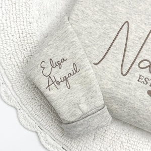 May include: Gray sweatshirt with the name "Eliza Abigail" embroidered on the sleeve and the word "Nora" embroidered on the front.