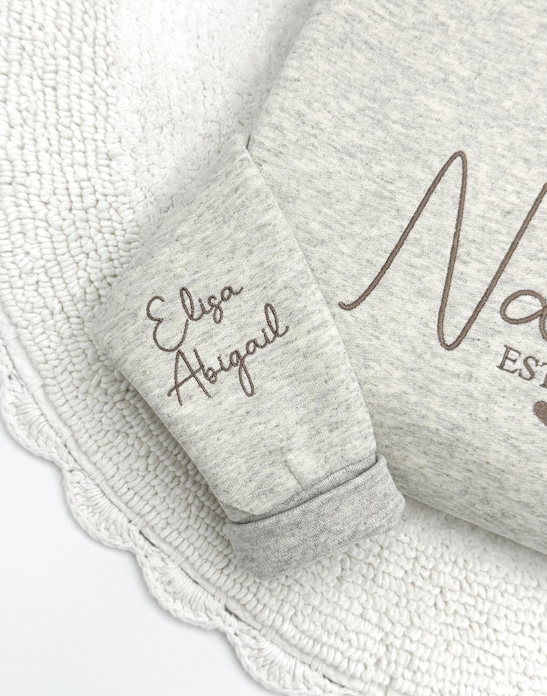 May include: Gray sweatshirt with the name "Eliza Abigail" embroidered on the sleeve and the word "Nora" embroidered on the front.