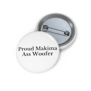 May include: Two white round buttons with metal pin backs. The front button has the text "Proud Makima Ass Woofer" in black, centered on the button. The second button is partially visible in the background.