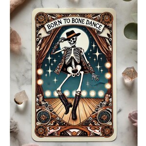 May include: A tarot card illustration featuring a dancing skeleton wearing a hat and boots, set against a backdrop of a stage with a full moon and stars. The text "BORN TO BONE DANCE" is displayed at the top.