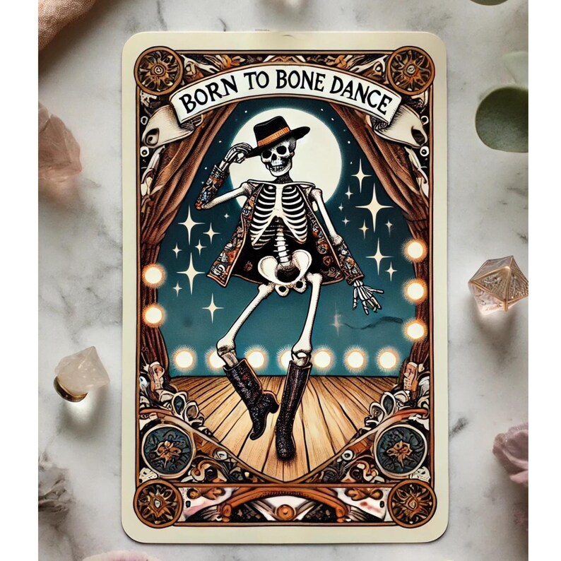 May include: A tarot card illustration featuring a dancing skeleton wearing a hat and boots, set against a backdrop of a stage with a full moon and stars. The text "BORN TO BONE DANCE" is displayed at the top.