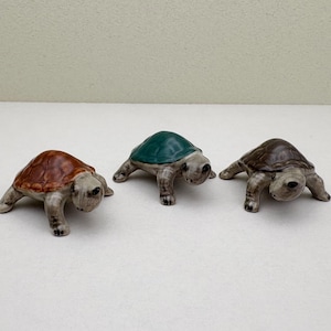 May include: Three ceramic turtle figurines. One turtle is brown, one is green, and one is gray.