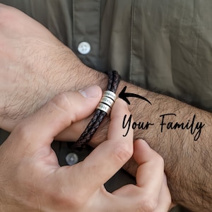 May include: A brown leather bracelet with silver beads engraved with the names "Matt", "Olivia", and "Keaton".