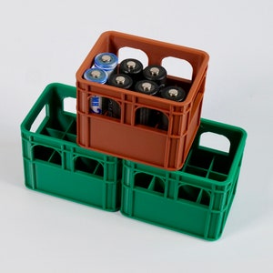 Könnte beinhalten: Zwei grüne Plastikkisten übereinander gestapelt. Eine braune Plastikkiste sitzt oben auf den grünen Kisten. Die braune Kiste ist mit AA-Batterien gefüllt.