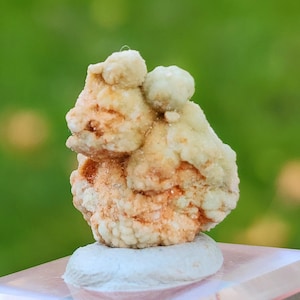 Può includere: Una piccola roccia di formazione naturale, di colore bianco e arancione, con una superficie ruvida e testurizzata. La roccia ha una forma organica unica e sembra essere un ammasso di cristalli più piccoli.