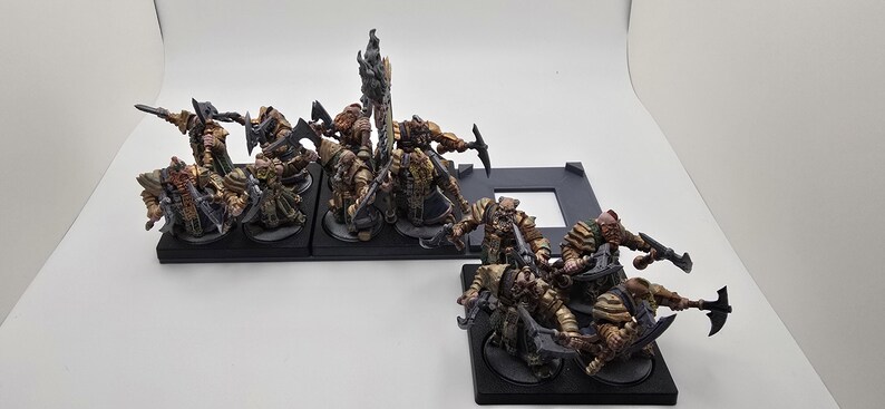 May include: A group of 12 painted miniature figures of warriors, each standing on a black base. The figures are wearing armor and carrying weapons, and they are arranged in a battle formation.