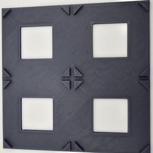 May include: A dark gray picture frame with four square openings. The frame has a decorative design with a cross in the center and triangles at the corners.